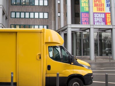 Gelbes Lieferfahrzeug vor Gebäude